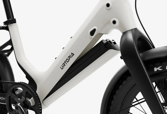 Side view of the Urtopia Carbon Joy Ultra eBike in a modern setting, showcasing its sleek carbon frame, integrated battery, and minimalist design.